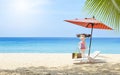 Miniature girl with pink swimsuit standing under umbrella on tropical beach