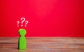 A miniature green man and question marks above him. Uncertainty. Search for an answer to a question. Problems and solutions Royalty Free Stock Photo