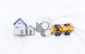 Miniature hosue with coins and front loader truck on white fabric background Royalty Free Stock Photo