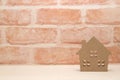 Miniature house in front of brick wall.