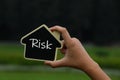 Miniature house in hands with text risk on it.