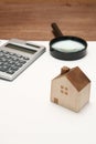 Miniature house, magnifying glass, calculator on blank notebook.