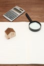 Miniature house, magnifying glass, calculator on blank notebook.