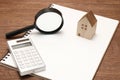 Miniature house, magnifying glass, calculator on blank notebook.