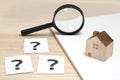 Miniature house and many question marks on white papers. House with question marks and magnifying glass. Real Estate Concept.