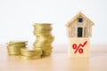 Small house on rising percent icon on wood cube and blurred stack of coins on wooden desk , for interest, increasing price