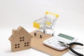 Miniature house, shopping cart, calculator and tools on white background. Concept of buying new house, real estate and renovation.