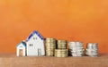 Miniature house and stack of silver and gold coins over blurred orange background Royalty Free Stock Photo