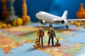 Miniature male and female travelers with backpacks stand near a world map and airplane model