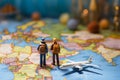 Miniature male and female travelers with backpacks stand near a world map and airplane model