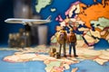 Miniature male and female travelers with backpacks stand near a world map and airplane model