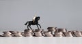 A miniature man riding horse on piles of coins.
