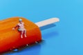 miniature man in swimsuit on a melting orange popsicle