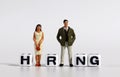 A miniature man and woman standing with a cube with a HIRING word.