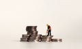 A miniature manual worker on a pile of coins.