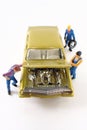 Miniature mechanics work on a gold toy car.