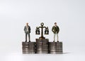 Miniature men standing on a pile of coins of the same height. Pile of coins and a miniature scale.
