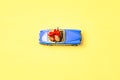 Miniature mini toy.Blue toy car with open top convertible carrying a gift with a red bow on a yellow background. View Royalty Free Stock Photo