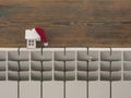 Miniature model house with knitted cap and scarf on heating radiator. Space for text. Saving heating in winter Royalty Free Stock Photo