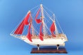 Miniature model of old ship with red sails on blue background Royalty Free Stock Photo