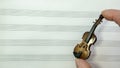 Fingers hold a miniature violin over the sheet music lines.