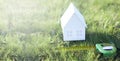 Miniature paper house on green grass in summer. Measuring tape or tape measure. The concept of buying a land plot for building a