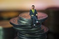 Miniature people Businessman sitting on coin stack warm background. Success Concept. Macro