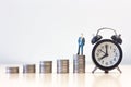 Miniature people businessman standing on Money coin stack with Alarm clock, Finance sustainable development concept