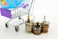 Miniature people: Businessman standing on stack of coins, shopping cart with world map for retail business. Image use for online
