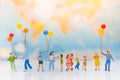 Miniature people: children hold balloons, and play together, background is map of world,