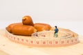 Miniature people : Close up fat man standing in waist tape measure and looking at sausages Royalty Free Stock Photo