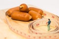 Miniature people : Close up fat man standing in waist tape measure and looking at sausages Royalty Free Stock Photo