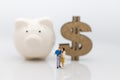 Miniature people : Couple standing area front of piggy bank and wooden dollar. Image use for Valentine`s day