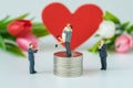 Miniature people with couple standing on top stack of coins and