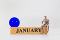 Miniature people, A dejected businessman is sitting on a wooden with Blue face emoji , Blue monday concept