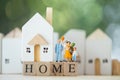 Miniature people: Family stand on wood block words HOME and house background. The concept of family values