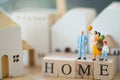 Miniature people: Family stand on wood block words HOME and house background. The concept of family values