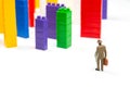 Miniature people. figures of people stand near the colored blocks of a plastic constructor on a white background in the form of Royalty Free Stock Photo