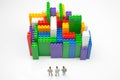 Miniature people. figures of people stand near the colored blocks of a plastic constructor on a white background in the form of Royalty Free Stock Photo