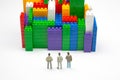 Miniature people. figures of people stand near the colored blocks of a plastic constructor on a white background in the form of Royalty Free Stock Photo