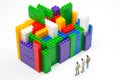 Miniature people. figures of people stand near the colored blocks of a plastic constructor on a white background in the form of Royalty Free Stock Photo