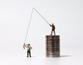 Miniature people fishing and piles of coins. The concept of income inequality. Royalty Free Stock Photo