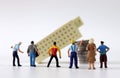 Miniature people gathered in front of miniature building falling on piles of coins.