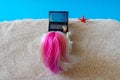 Miniature people girl with pink hair sits in a deck chair with a laptop and a glass of drink in her hands and looks at the sea.