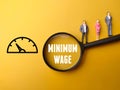 Miniature people, magnifying glass and icon with text MINIMUM WAGE