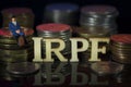 Miniature People. Man sitting on coin stacks with Text. IRPF Taxman Concept. Macro Royalty Free Stock Photo