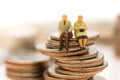 Miniature people, Old couple figure sitting on top of stack coin Royalty Free Stock Photo