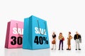 Miniature people - people standing in front of paper bags with printed big sale.