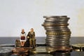 Miniature people seniors sitting on stack coins