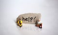 Miniature people sitting in front of a piece of paper with the text `help!` Royalty Free Stock Photo